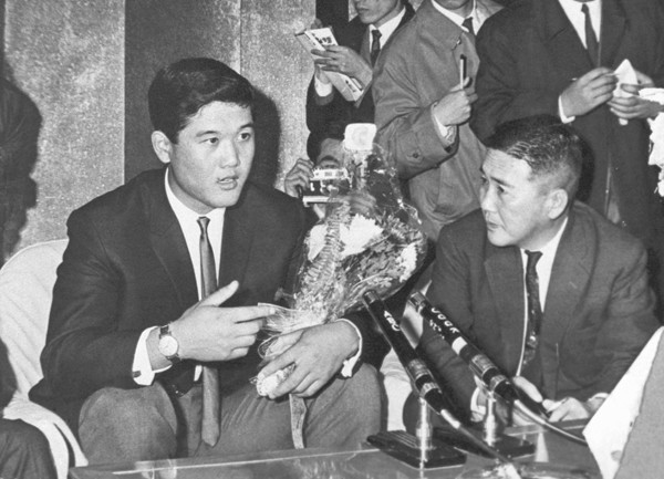 1964年12月16日、羽田空港でアメリカからの帰国記者会見に臨む村上さん（写真＝共同通信）