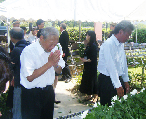 被爆70周年の慰霊祭式典に出席した今西氏（左）。献花台の前で手を合わせる