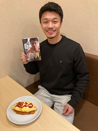 書籍を手に、「超える」と書かれたオムライスと