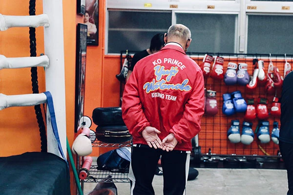 中屋トレーナーが着る赤いジャンパーの背中には、かつての愛弟子の名前が入っている